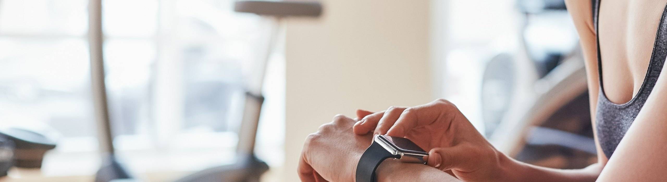 A woman checks the sports tech smartwatch on her wrist during a workout in a gym